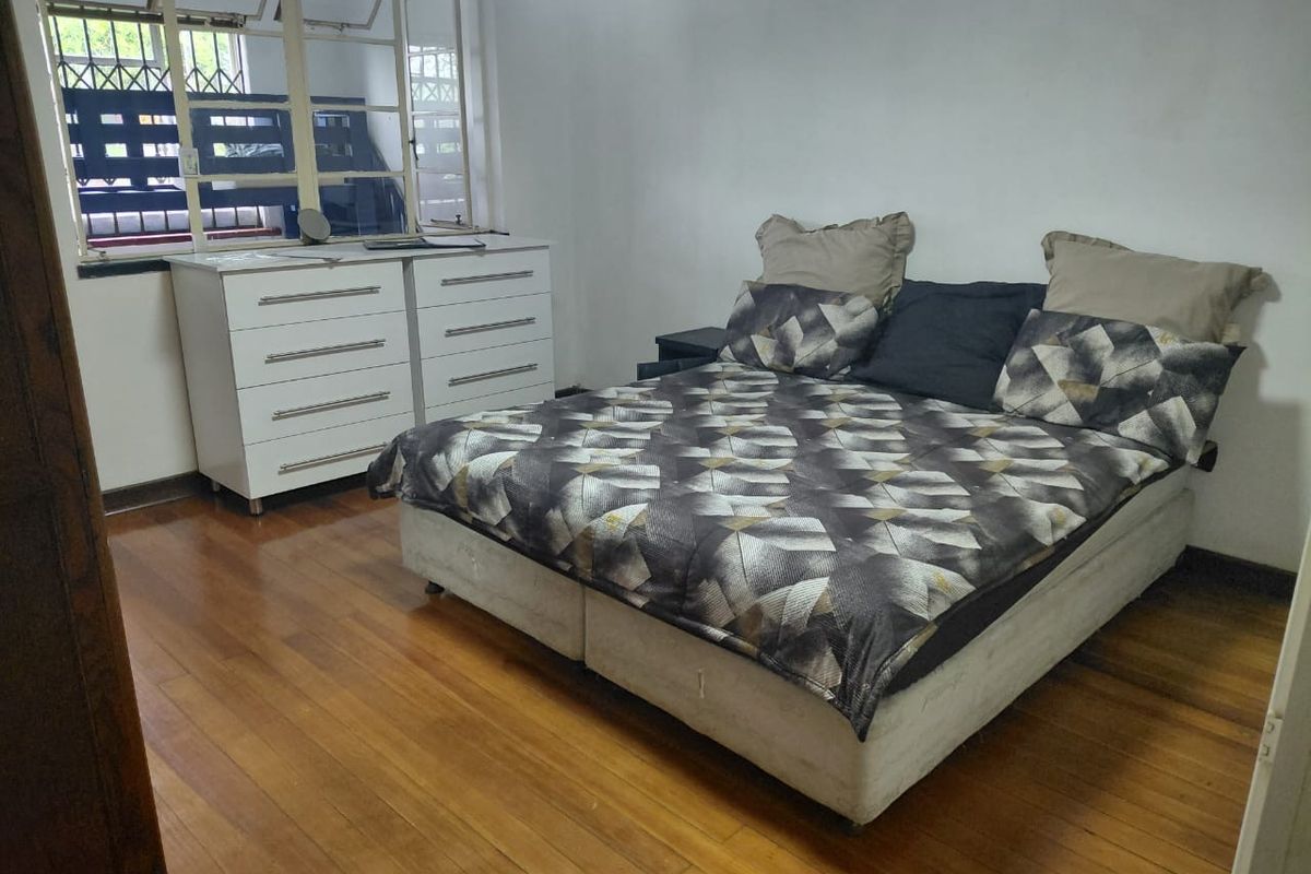 A bedroom featuring polished wooden flooring and a large window with security bars.