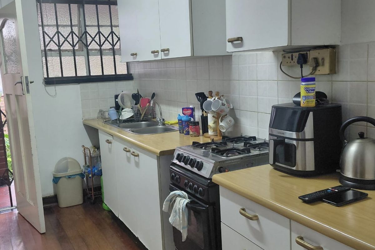 A functional kitchen featuring white cabinetry, laminate countertops, a gas stove, and a double basin sink with a security-barred window.