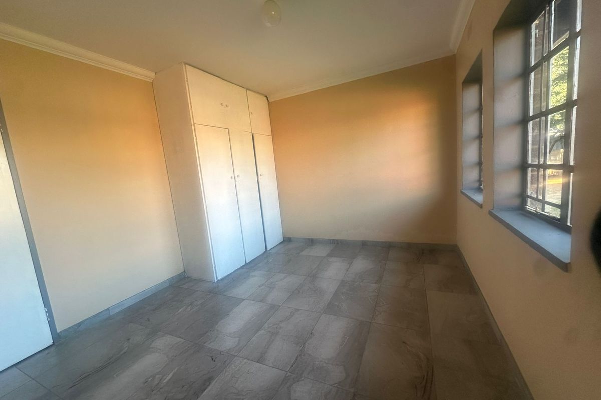 A vacant bedroom featuring tiled flooring, built-in cupboards, and steel-framed windows, offering a clean and neutral space ready for personalization.