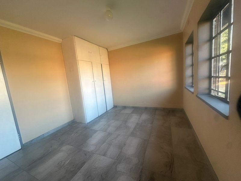 A vacant bedroom featuring tiled flooring, built-in cupboards, and steel-framed windows, offering a clean and neutral space ready for personalization.