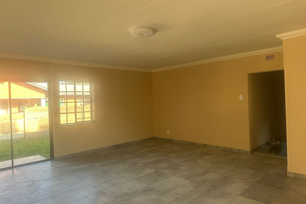 A spacious, empty living room featuring neutral walls, tiled flooring, and a sliding glass door providing access to the exterior.
