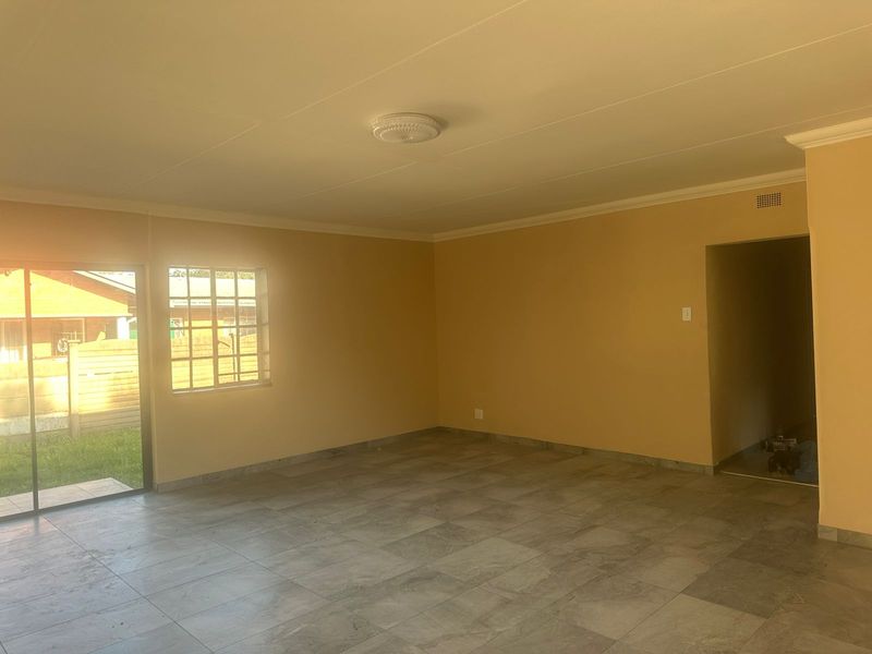 A spacious, empty living room featuring neutral walls, tiled flooring, and a sliding glass door providing access to the exterior.