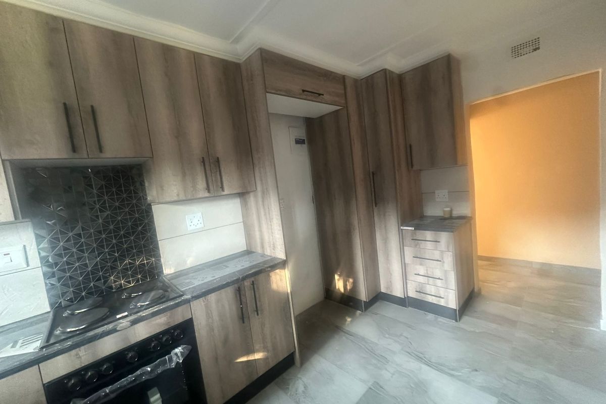 Modern kitchen featuring wood-look cabinetry, tiled backsplash, built-in oven and stove, and neutral floor tiles in a clean, empty space.
