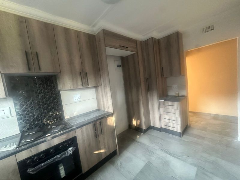 Modern kitchen featuring wood-look cabinetry, tiled backsplash, built-in oven and stove, and neutral floor tiles in a clean, empty space.
