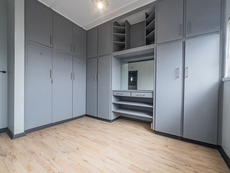 A bright bedroom featuring extensive grey built-in cabinetry, a central vanity area, and light wood-look laminate flooring.