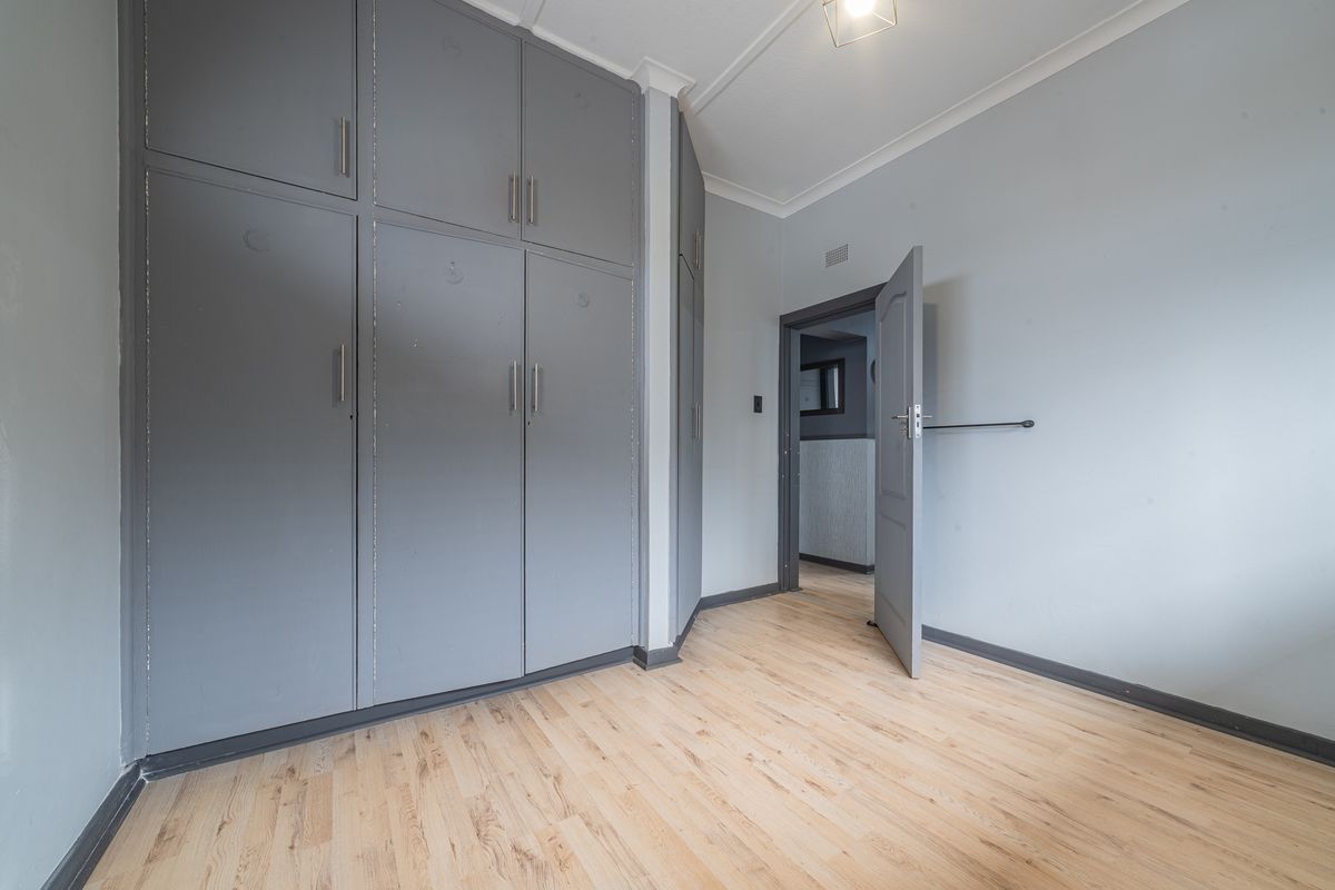 A vacant bedroom featuring light laminate flooring and extensive grey built-in cupboards, offering a neutral canvas for personalization.