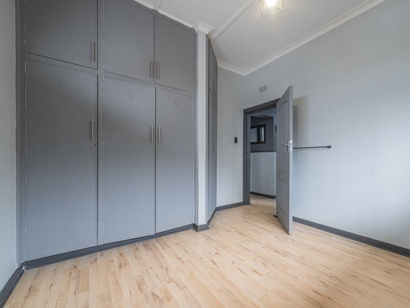 A vacant bedroom featuring light laminate flooring and extensive grey built-in cupboards, offering a neutral canvas for personalization.