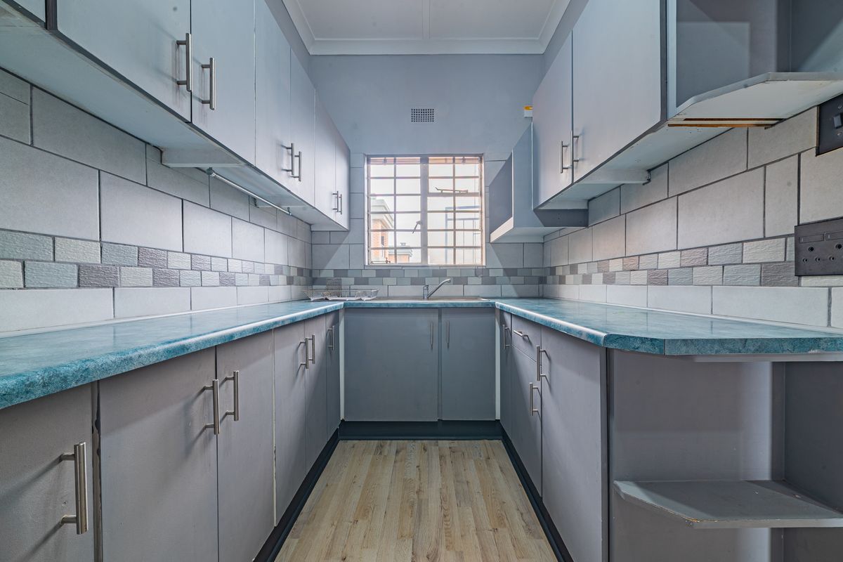 A compact, empty kitchen featuring grey built-in cabinetry, blue laminate countertops, tiled backsplash, and wood-look laminate flooring.
