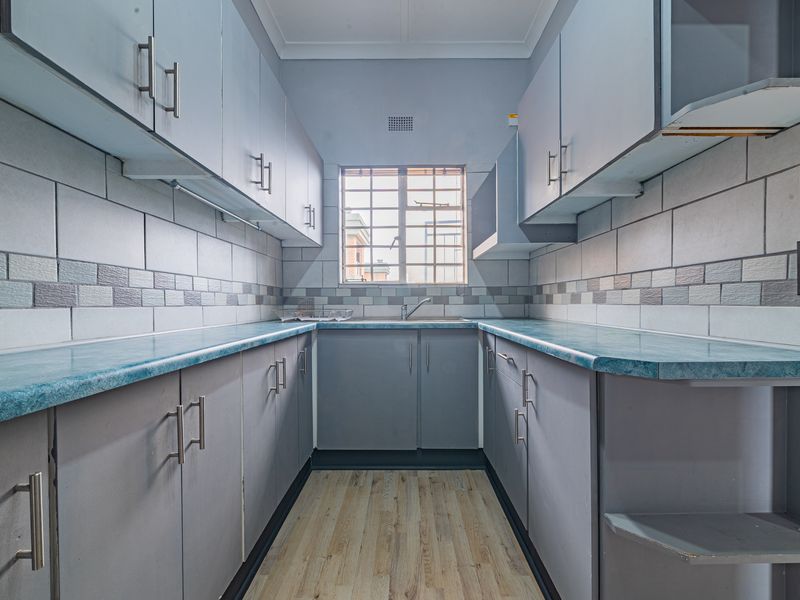 A compact, empty kitchen featuring grey built-in cabinetry, blue laminate countertops, tiled backsplash, and wood-look laminate flooring.