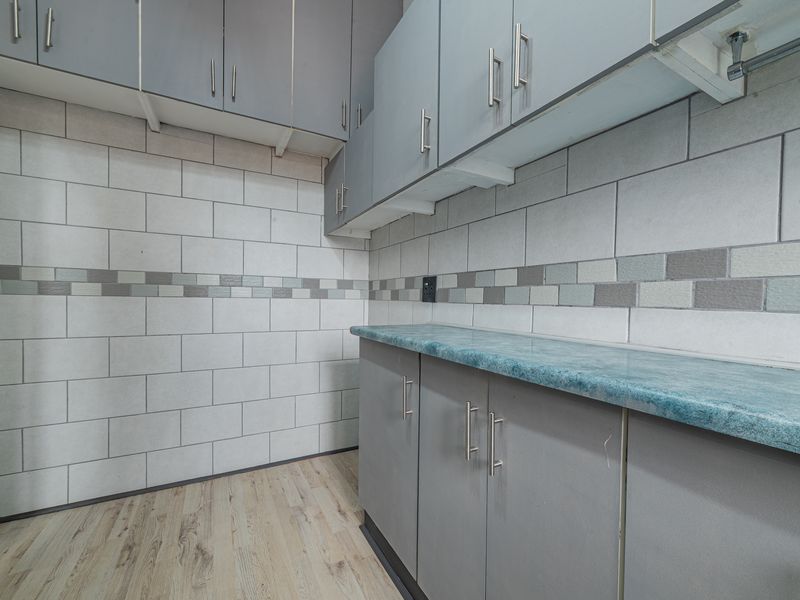 A clean and functional laundry area featuring ample built-in grey cabinetry, a durable laminate countertop, and modern tiled backsplash.