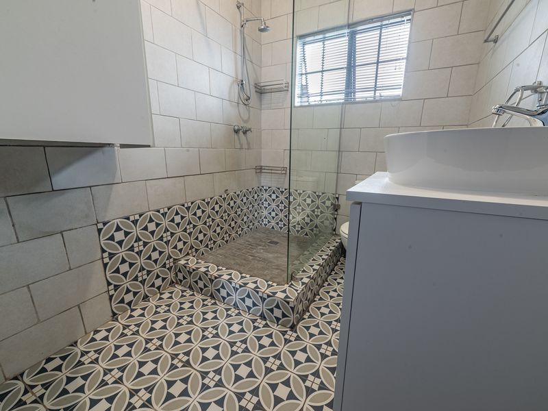 A modern bathroom featuring a walk-in shower with a glass screen, patterned floor tiles, and a contemporary vanity with a vessel sink.