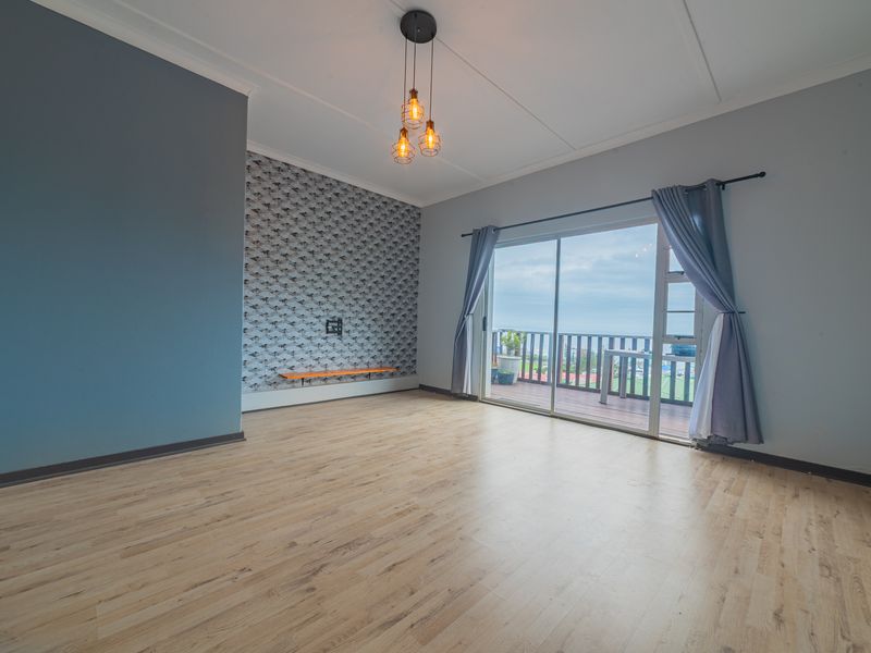 Spacious living area featuring light laminate flooring, a feature wallpaper wall with a floating shelf, and sliding glass doors leading to a balcony.