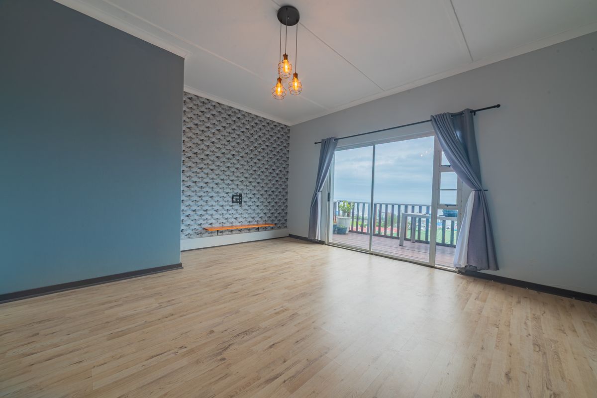 Spacious living area featuring light laminate flooring, a feature wallpaper wall with a floating shelf, and sliding glass doors leading to a balcony.