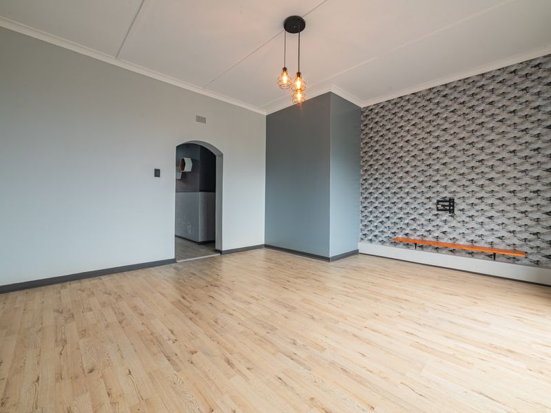 A bright and spacious living room featuring light laminate flooring, a decorative feature wall, and a classic arched doorway leading to an adjacent space.