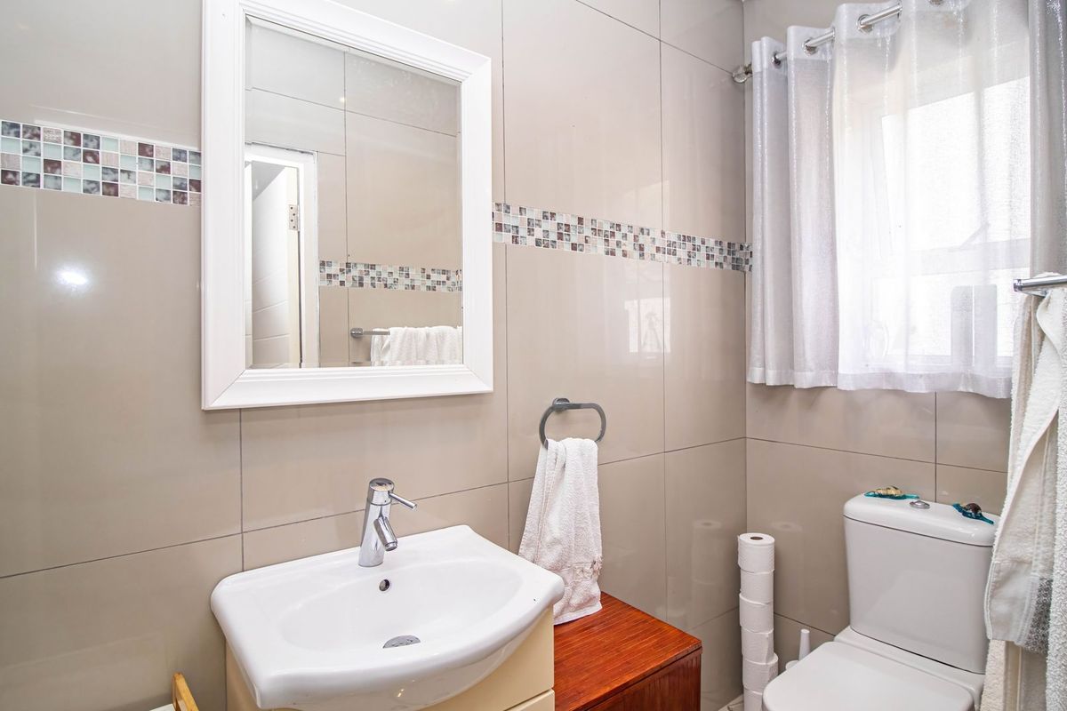 A well-maintained bathroom featuring neutral ceramic wall tiles with a decorative mosaic border, a vanity basin, and a standard toilet.