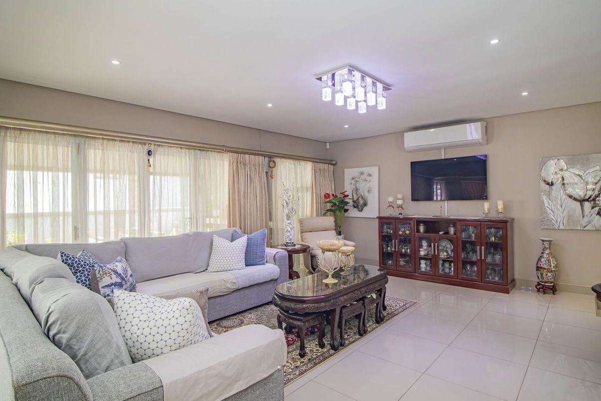 A well-maintained living room featuring tiled flooring, recessed downlighting, a modern chandelier, and a wall-mounted split-system air conditioner.