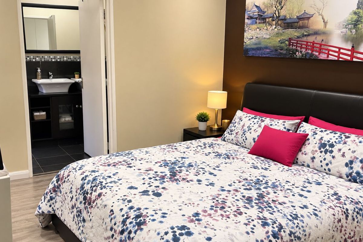 A well-maintained bedroom featuring laminate flooring and an adjoining en-suite bathroom with a modern vessel sink and vanity.