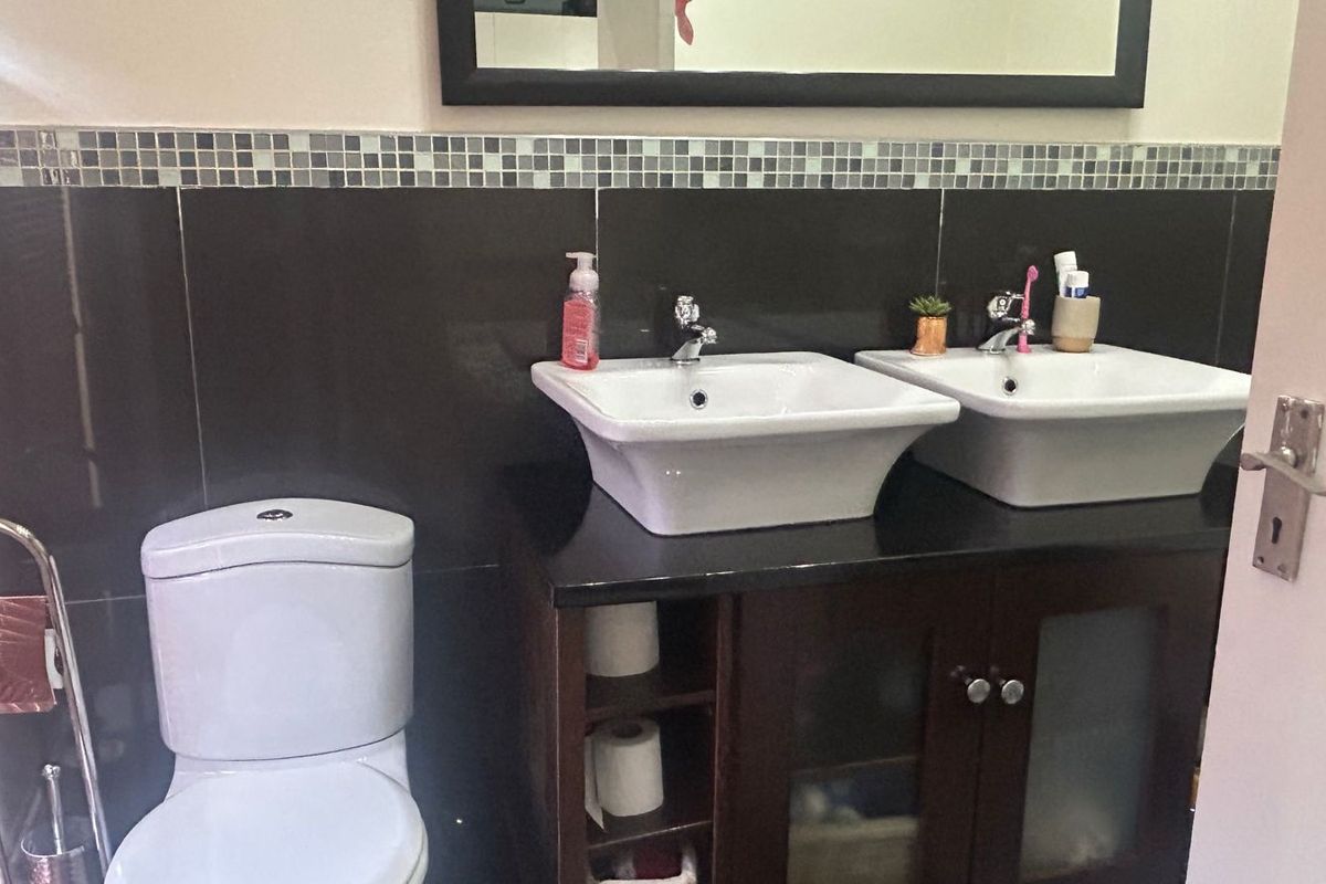 A bathroom featuring a double vanity with vessel sinks, dark cabinetry, and a tiled splashback with a wall-mounted mirror.