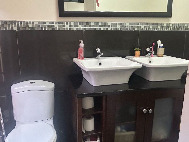 A bathroom featuring a double vanity with vessel sinks, dark cabinetry, and a tiled splashback with a wall-mounted mirror.