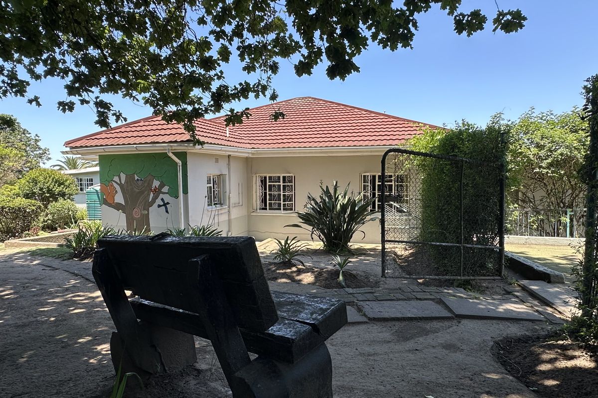 Rear view of the house featuring a tiled roof, security window bars, and a garden area with a metal gate.