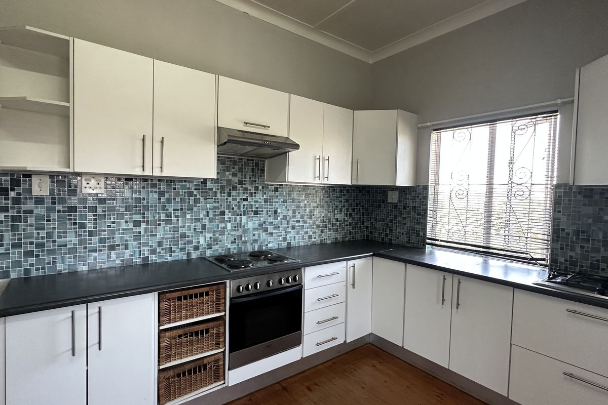 A functional kitchen featuring white cabinetry, mosaic tile backsplash, built-in oven and hob, and timber flooring, offering a solid foundation for modern updates.