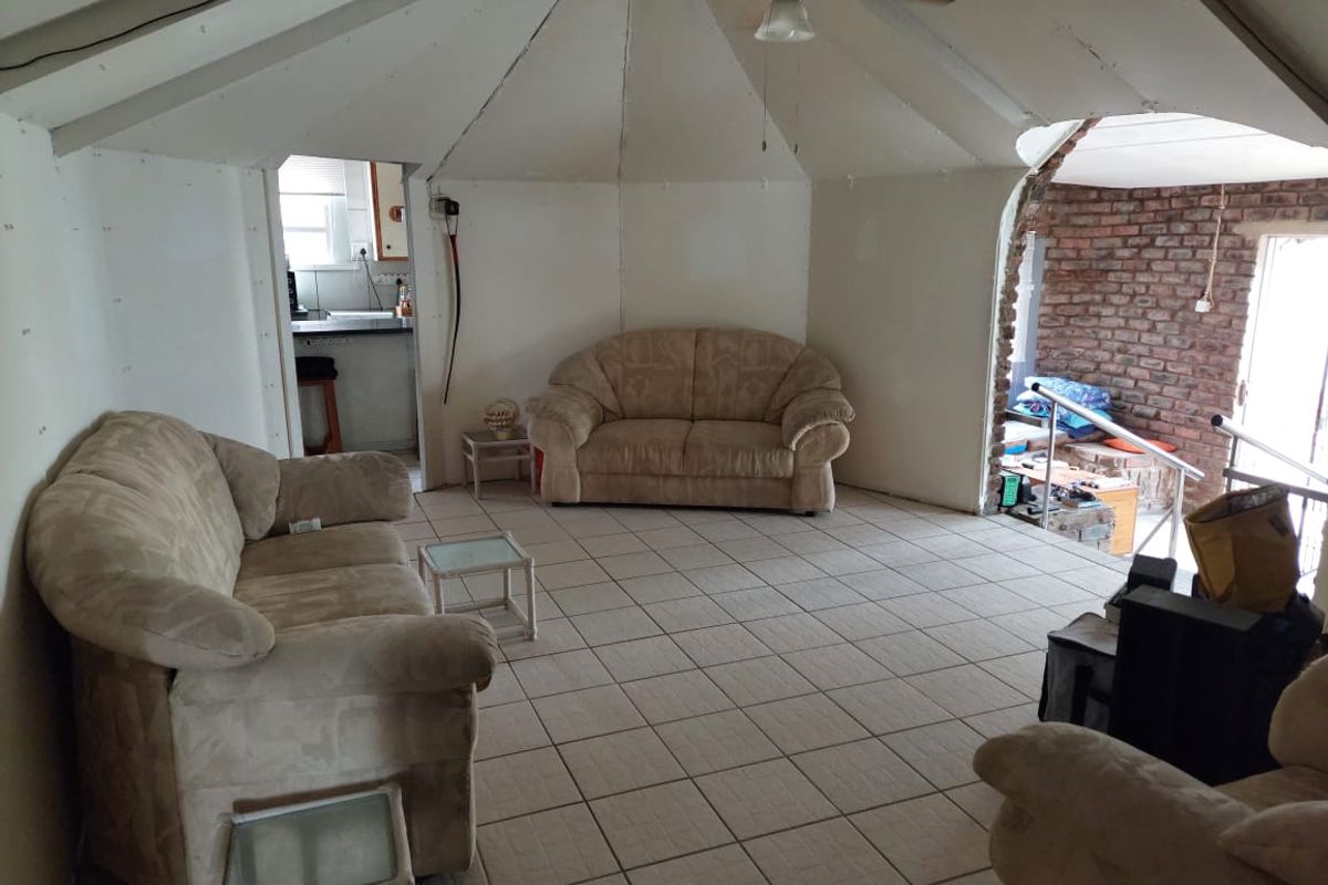 Spacious living area featuring a vaulted ceiling, tiled flooring, and an exposed brick feature wall, currently requiring finishing work on the wall panels.