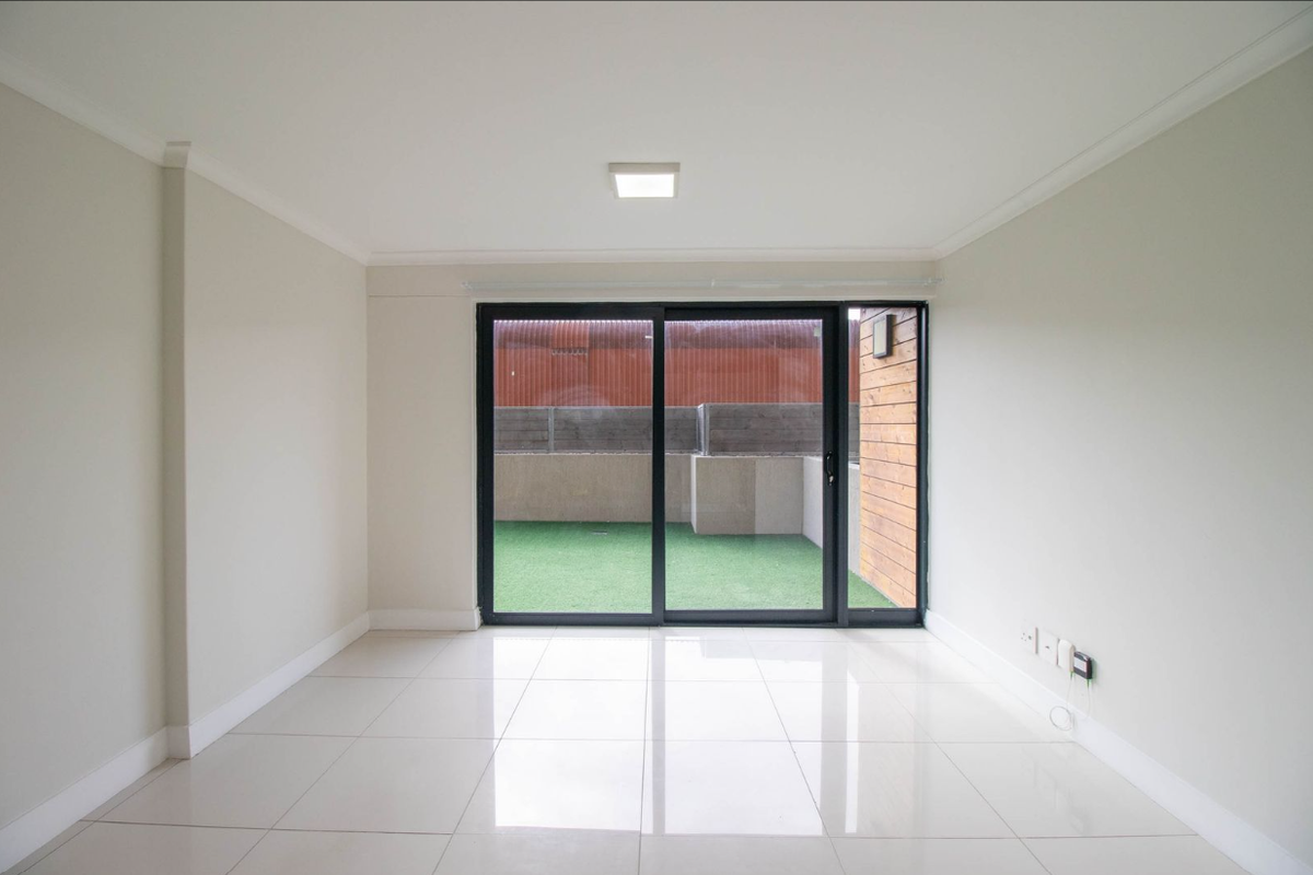 A bright, empty living room featuring neutral walls, polished tile flooring, and a large sliding glass door providing access to an outdoor patio area.