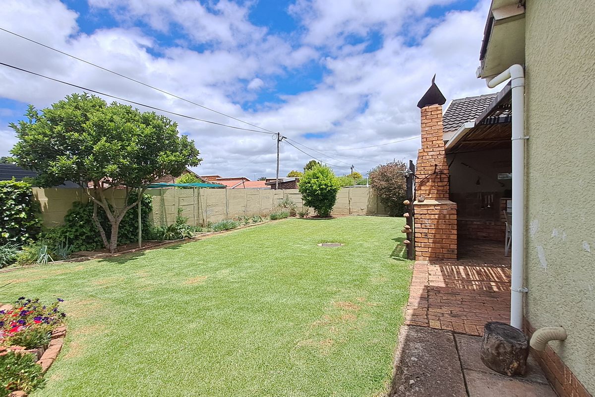 Rear garden featuring a well-maintained lawn, paved patio area, and a traditional brick built-in braai structure.