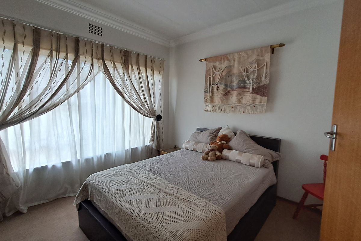 A bedroom featuring neutral carpeting, white walls, and a large window with curtain treatments.