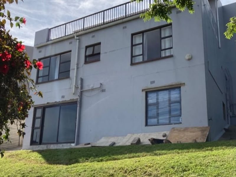 Rear elevation of a multi-story house featuring a rooftop terrace, aluminium window frames, and a sliding glass door, set against a sloped lawn.