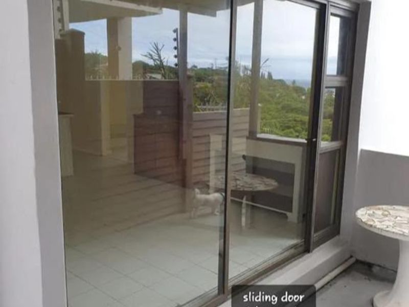 A covered patio area featuring a large sliding glass door with an integrated security gate, overlooking a garden and distant landscape.