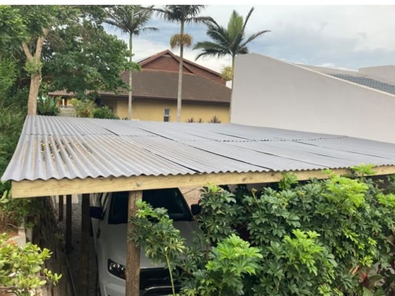 An outdoor carport structure featuring a corrugated metal roof supported by timber posts, providing covered parking space.