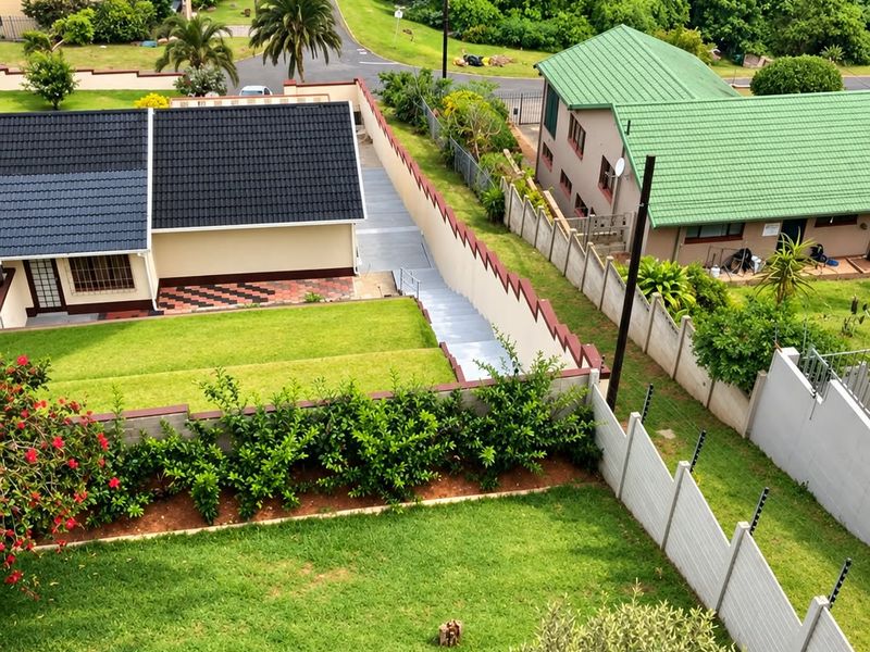 Aerial view of the property grounds, featuring a well-maintained lawn, boundary walls with electric fencing, and paved access paths within a residential neighborhood.