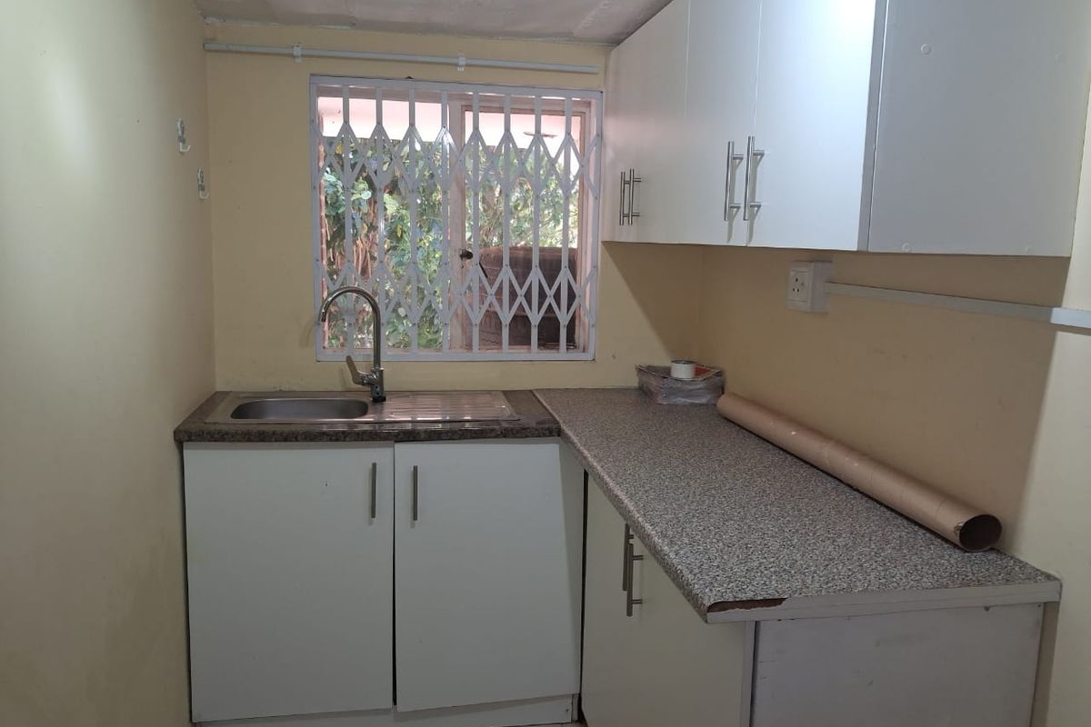 A compact kitchen featuring white cabinetry, a stainless steel sink, and a laminate countertop with a security gate on the window.