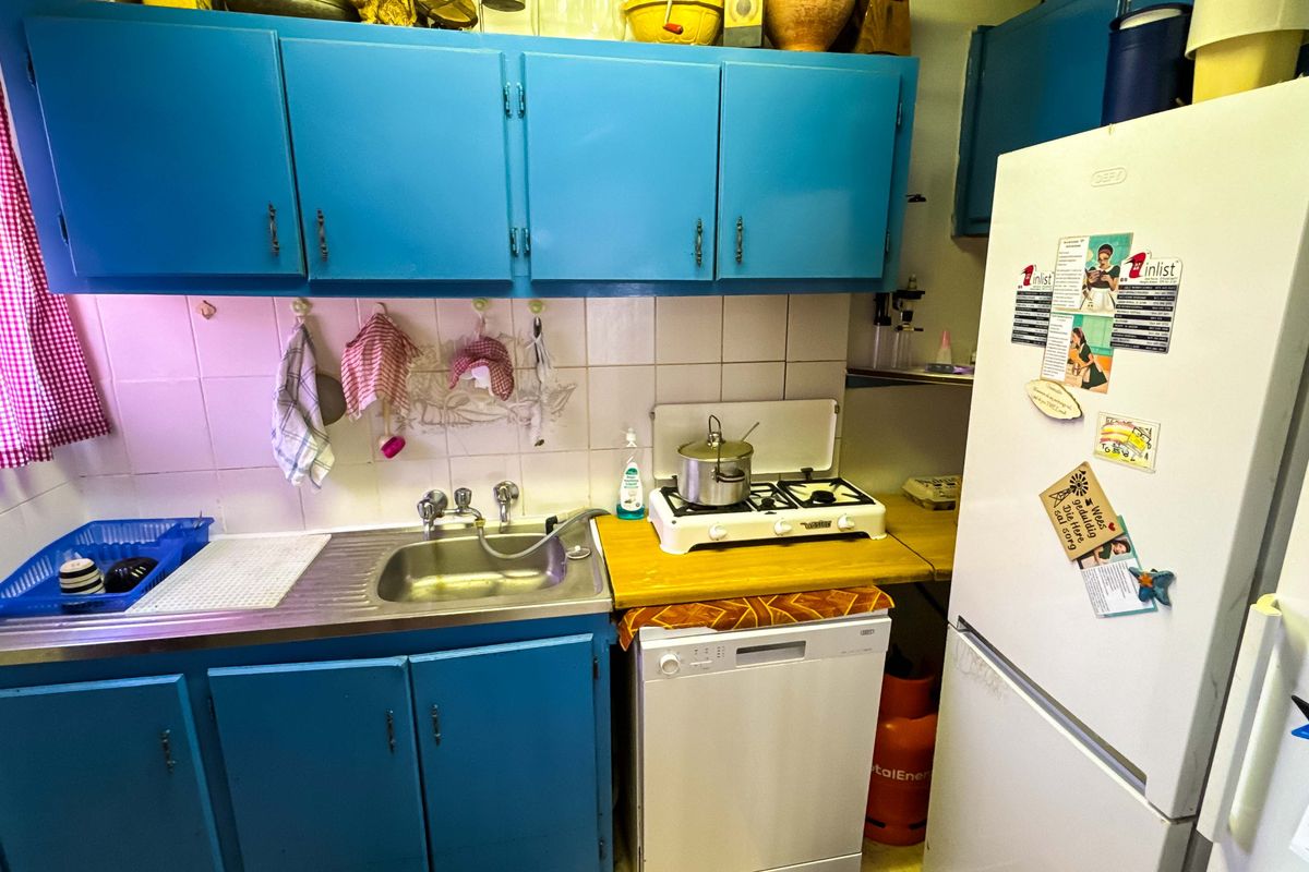 A compact kitchen featuring blue cabinetry, a stainless steel sink, tiled backsplash, and a gas cooktop, offering a functional but dated workspace.