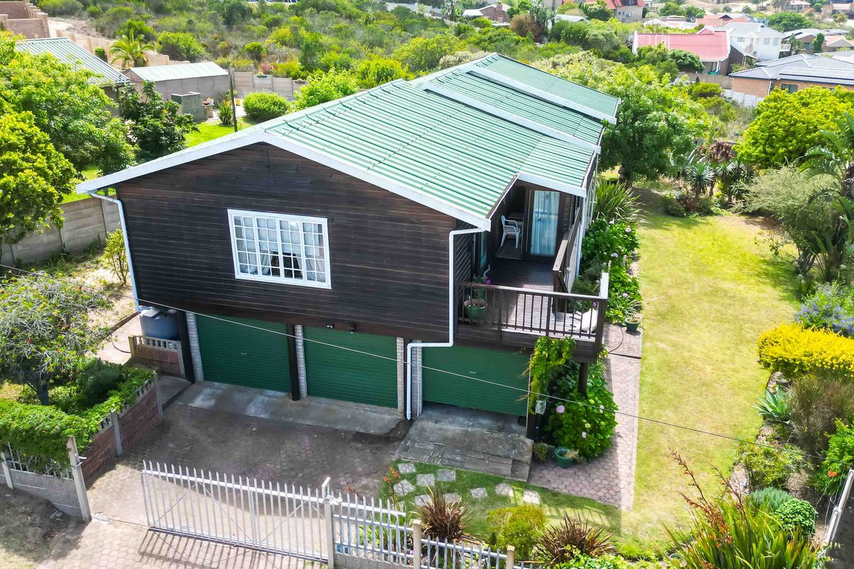 Aerial view of a detached house featuring a green corrugated roof, timber cladding, a triple garage, and a raised wooden deck set in a garden.