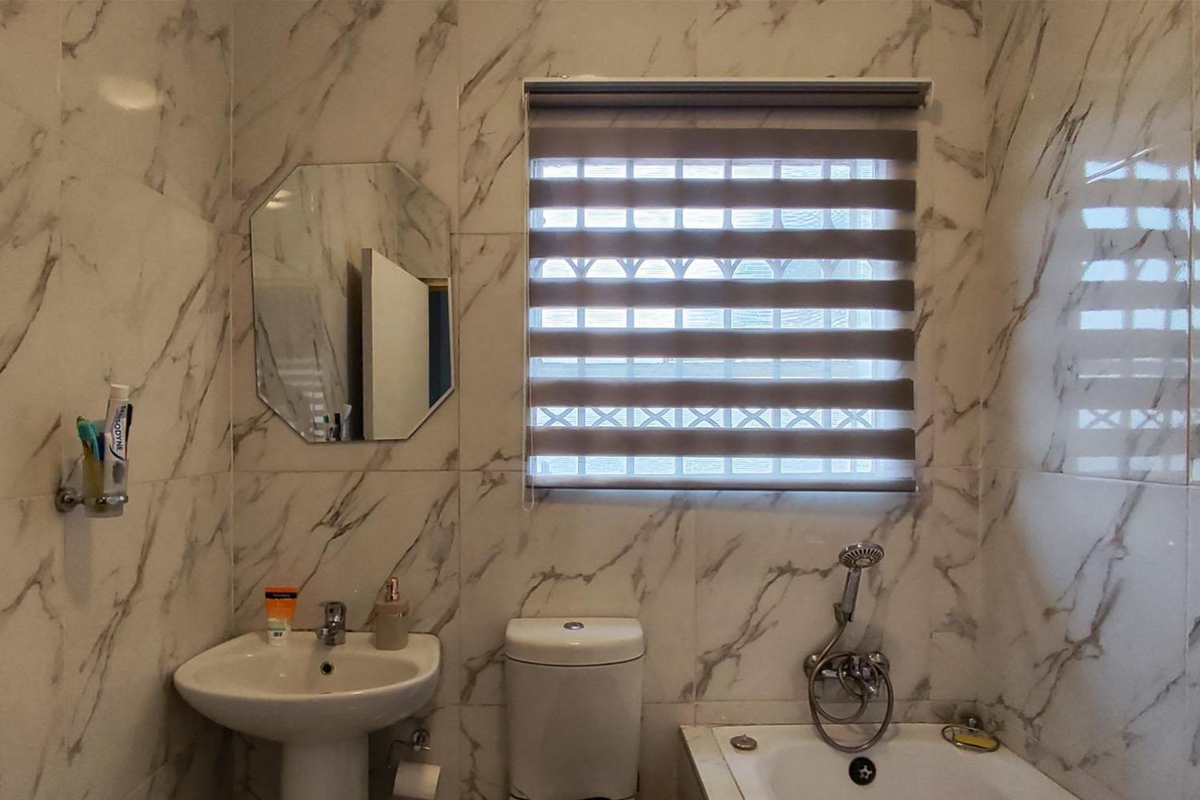 A well-maintained bathroom featuring marble-look wall tiles, a pedestal basin, a toilet, and a bathtub with a handheld shower attachment.