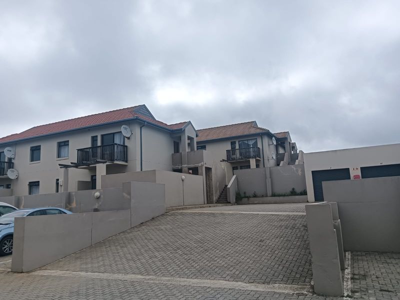 Exterior view of an apartment complex featuring paved driveway access, multiple balconies, and integrated garage units under a tiled roof.