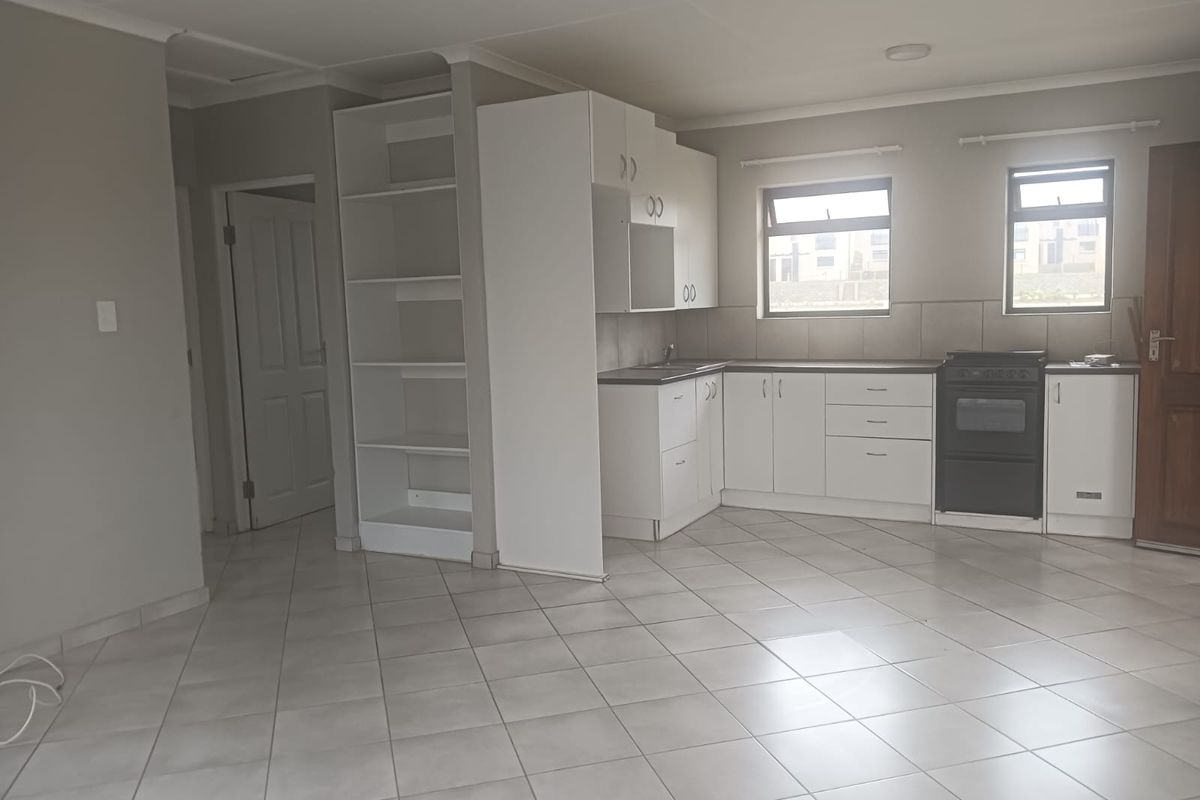A functional kitchen area featuring white cabinetry, tiled flooring, a built-in shelving unit, and a freestanding oven, presented in a clean, empty space.
