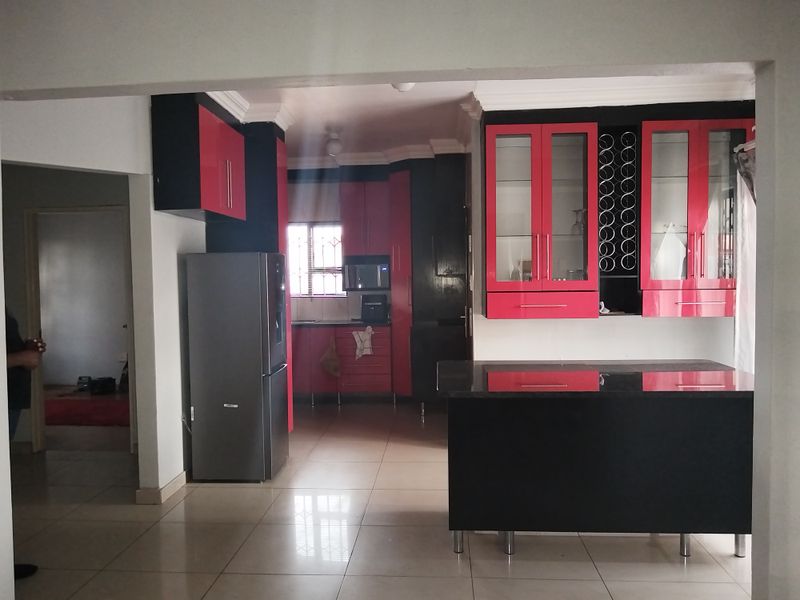 A kitchen featuring high-contrast red and black cabinetry, a central island, and tiled flooring, offering a modern layout with integrated storage solutions.