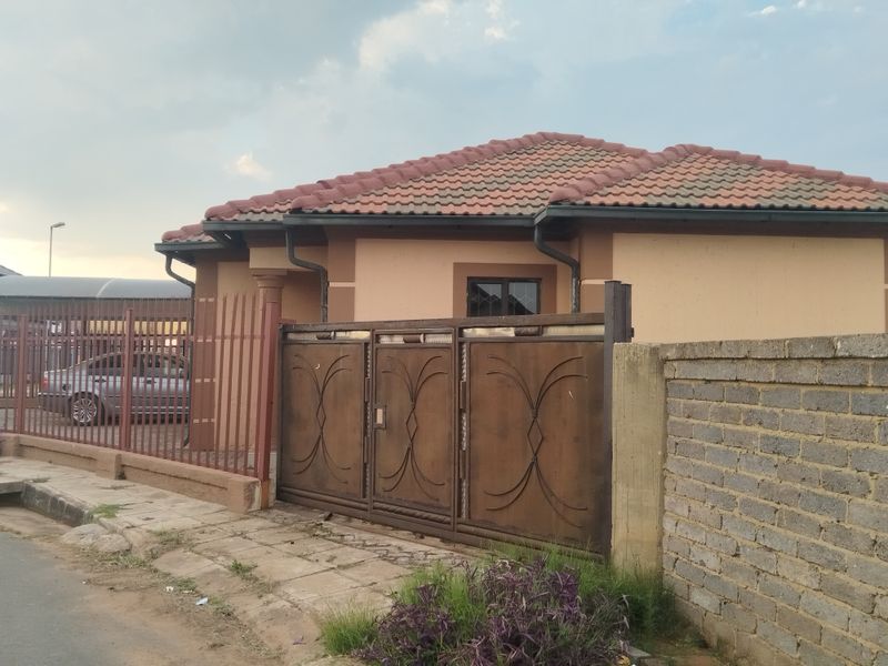 Front exterior view of a single-story house featuring a tiled roof, metal perimeter fencing, and a secure metal driveway gate.