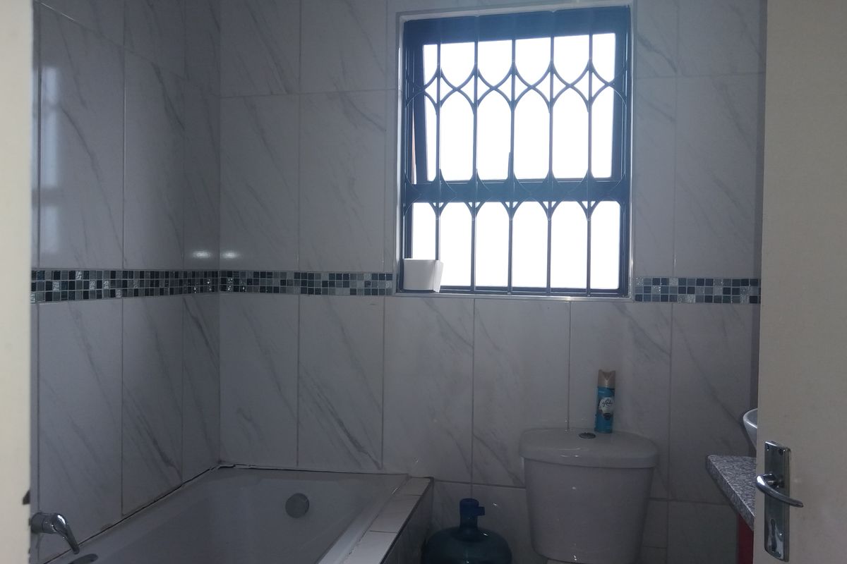 A functional bathroom featuring tiled walls, a built-in bathtub, a toilet, and a vanity unit with a security gate on the window.