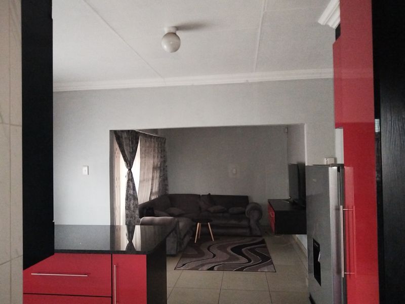 An open-plan living area featuring a kitchen with high-gloss red cabinetry and granite countertops, flowing into a comfortable lounge space with tiled flooring.