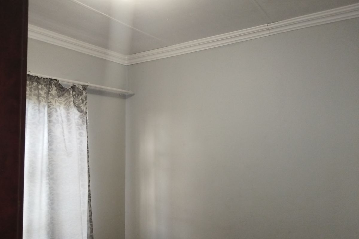 A simple, neutral-toned bedroom featuring ceiling cornicing and a window with curtain rail.