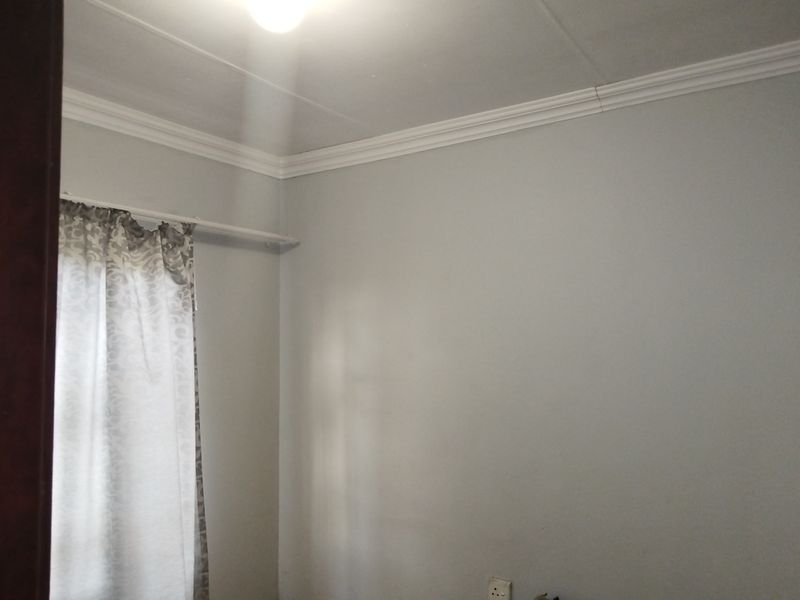 A simple, neutral-toned bedroom featuring ceiling cornicing and a window with curtain rail.