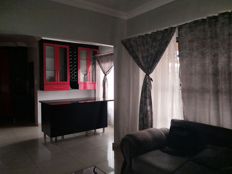 Open plan living area featuring tiled flooring, coved ceilings, and a built-in bar or cabinetry unit with red and black finishes.