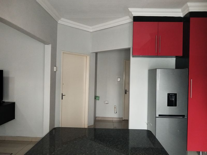 A kitchen area featuring red high-gloss cabinetry, a dark granite countertop, and tiled flooring with neutral wall finishes.