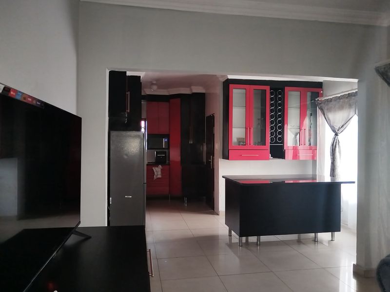 Open plan living area featuring a kitchen with high-contrast red and black cabinetry, a central island, and tiled flooring throughout.