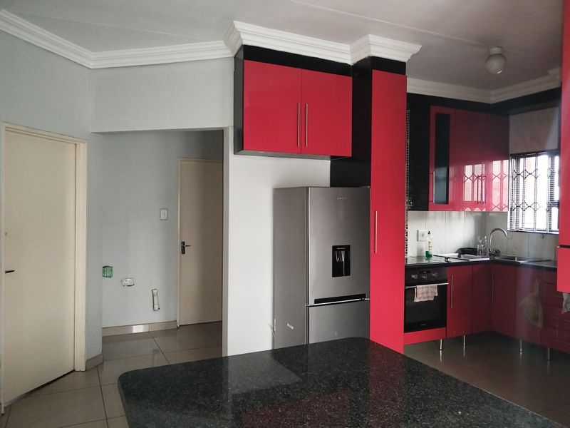 A functional kitchen featuring high-contrast red and black cabinetry, granite countertops, built-in oven, and tiled flooring, offering a modern layout with potential for cosmetic updates.