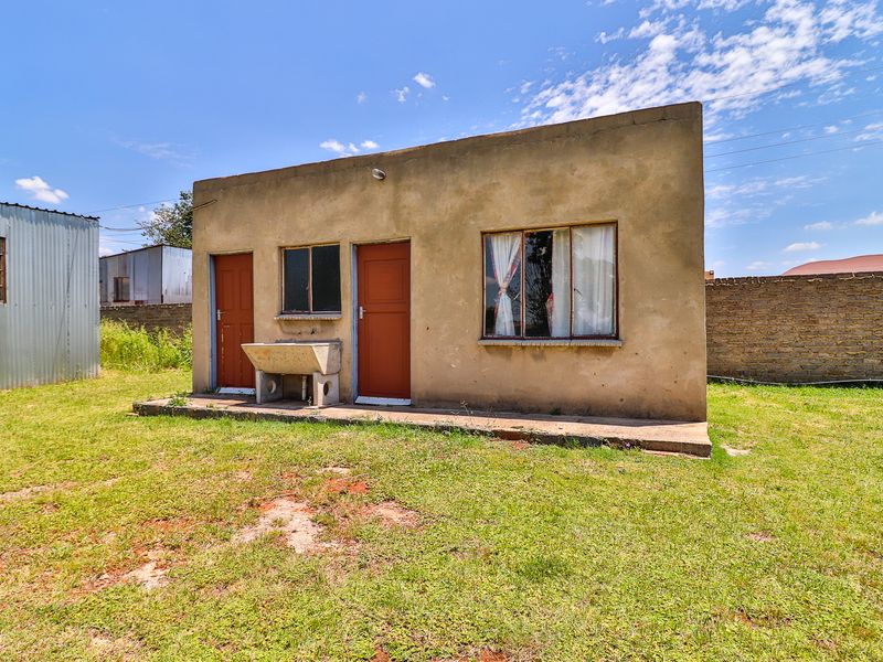 A detached outbuilding featuring a concrete utility sink, metal window frames, and a simple plaster finish, situated in a grassed backyard area.